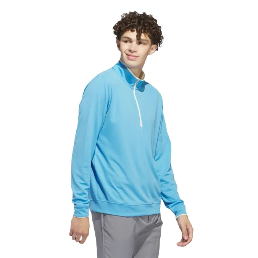 A young man with curly hair wears the Adidas Lightweight Half-Zip Top in light blue and gray pants, standing against a white background and looking to the side with a slight smile.