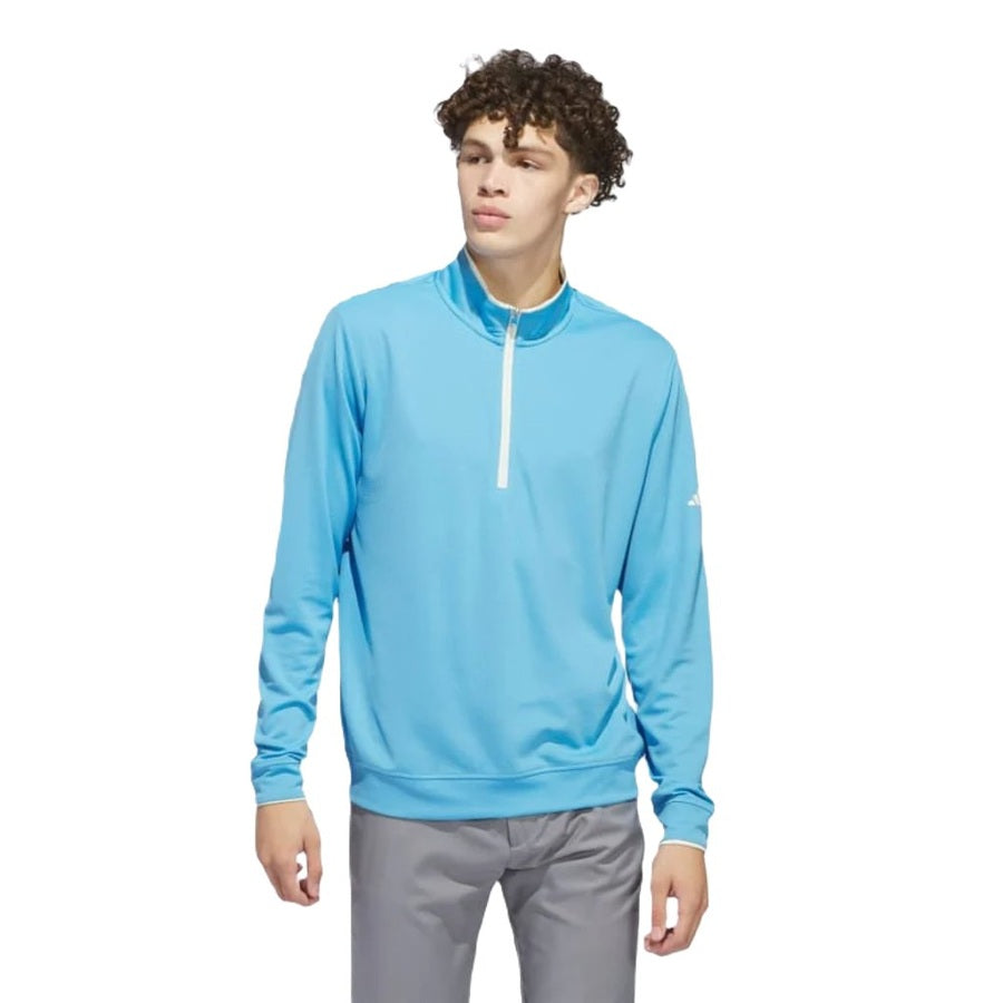 A young man wears the Adidas Lightweight Half-Zip Top - Final Sale in light blue, made from recycled materials, with gray pants, standing against a white background and looking to the side.