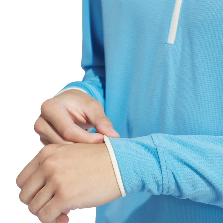 A person adjusts the cuff of their Adidas Lightweight Half-Zip Top—Final Sale, a light blue recycled-material golf top. The focus is on their hands and sleeves against a white background.