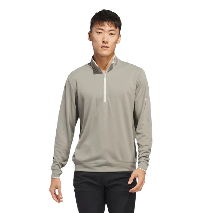 A young man stands facing forward against a white background, wearing the Adidas Lightweight Half-Zip Top—Final Sale, in light gray, paired with black pants.