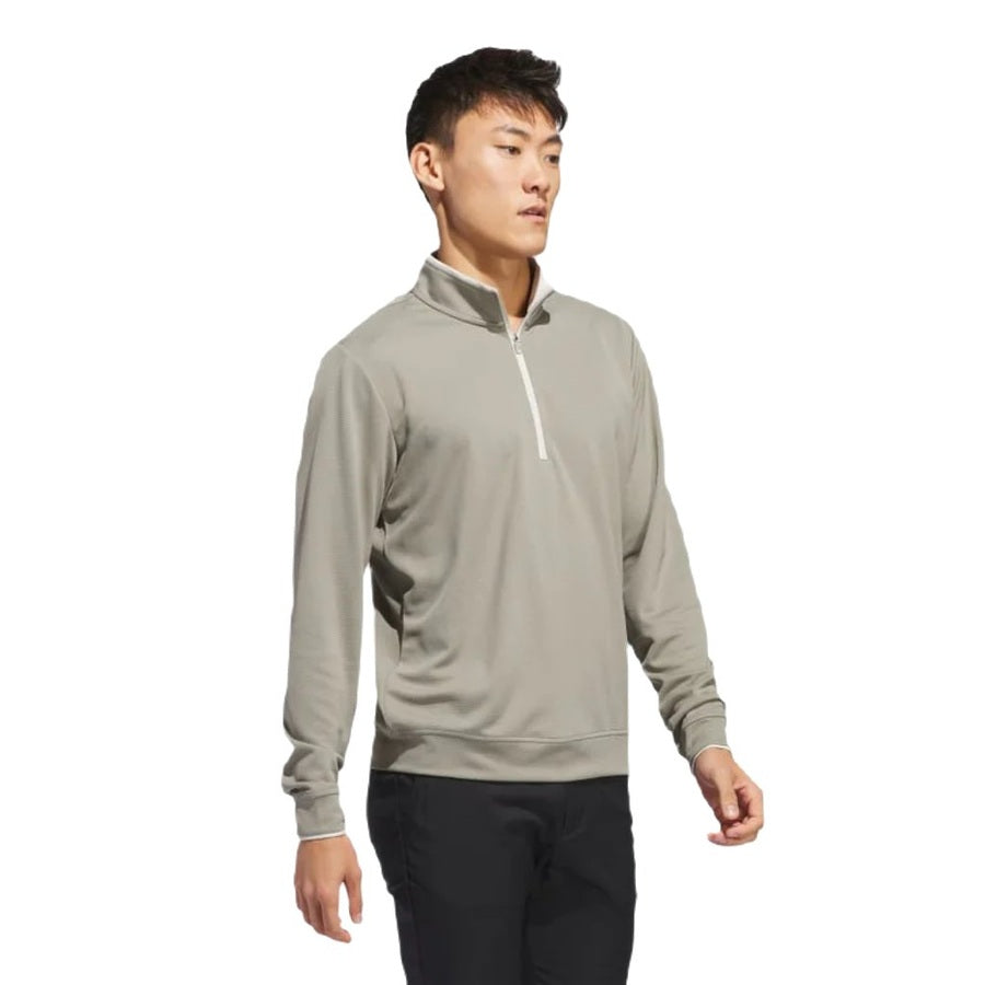 A man stands slightly sideways against a white background, wearing an Adidas Lightweight Half-Zip Top in light gray with black pants.