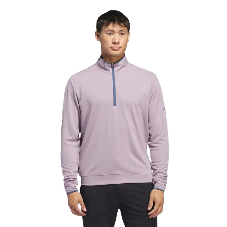 A man wears the Adidas Lightweight Half-Zip Top—light purple with a blue zipper, made from recycled materials—standing against a plain white background.