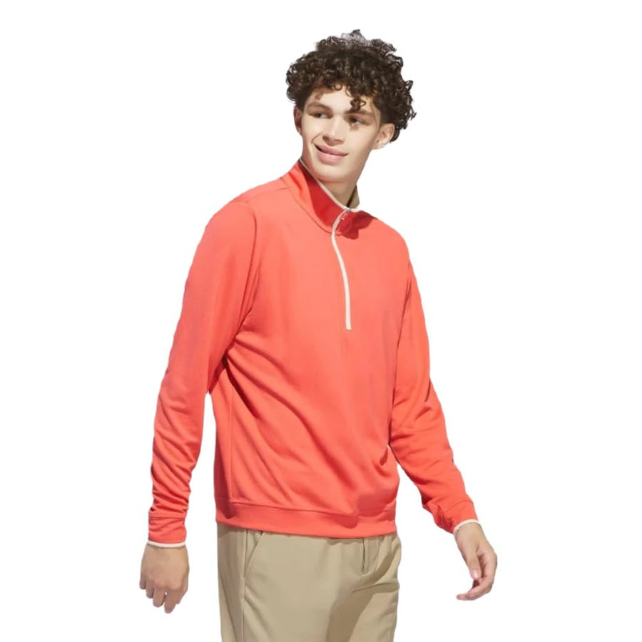 A young man with curly hair wears the Adidas Lightweight Half-Zip Top in bright coral and tan pants, standing against a white background and looking slightly to the side with a relaxed expression.