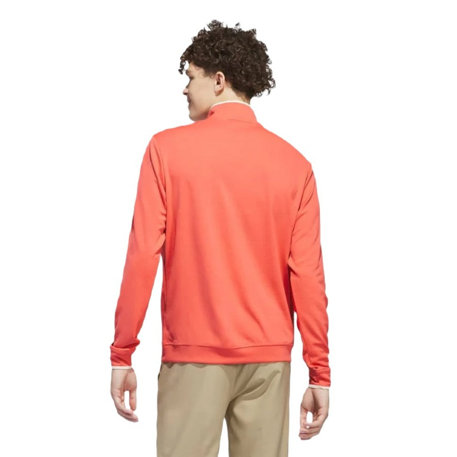 A person with curly hair is shown from behind wearing the Adidas Lightweight Half-Zip Top in bright coral and beige pants, against a plain white background.