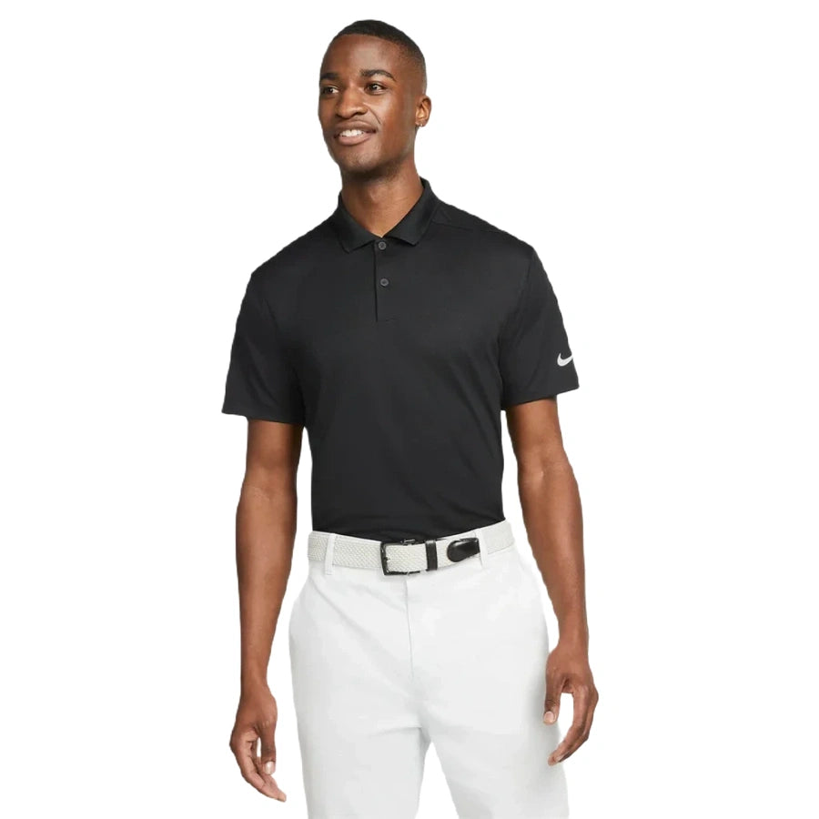 A man smiles in the Nike Dri-FIT Victory Men's Golf Shirt - Course/Event Logo (Final Sale), styled with white pants and a woven belt, showcasing its classic look against a plain white background.