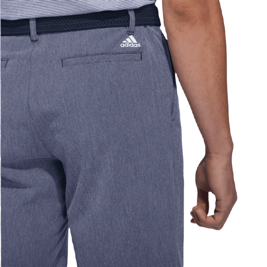 A person is seen from behind, waist down, wearing Adidas Crosshatch Shorts in blue with the logo above the back pocket, paired with a navy woven belt and a tucked-in striped shirt.