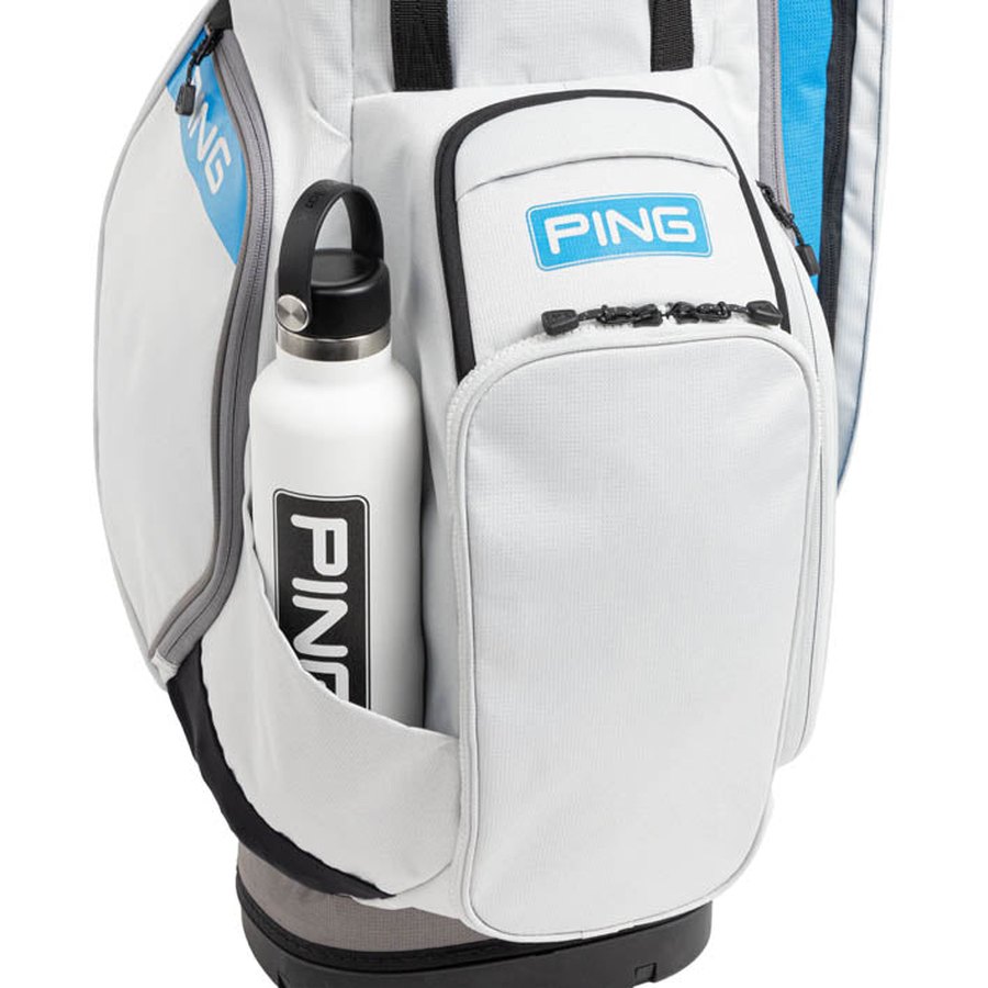 A close-up of the lightweight Ping Hoofer 231 Golf Carry Bag in white, featuring a large zippered pocket and a side holder with a white water bottle, both displaying the PING logo.