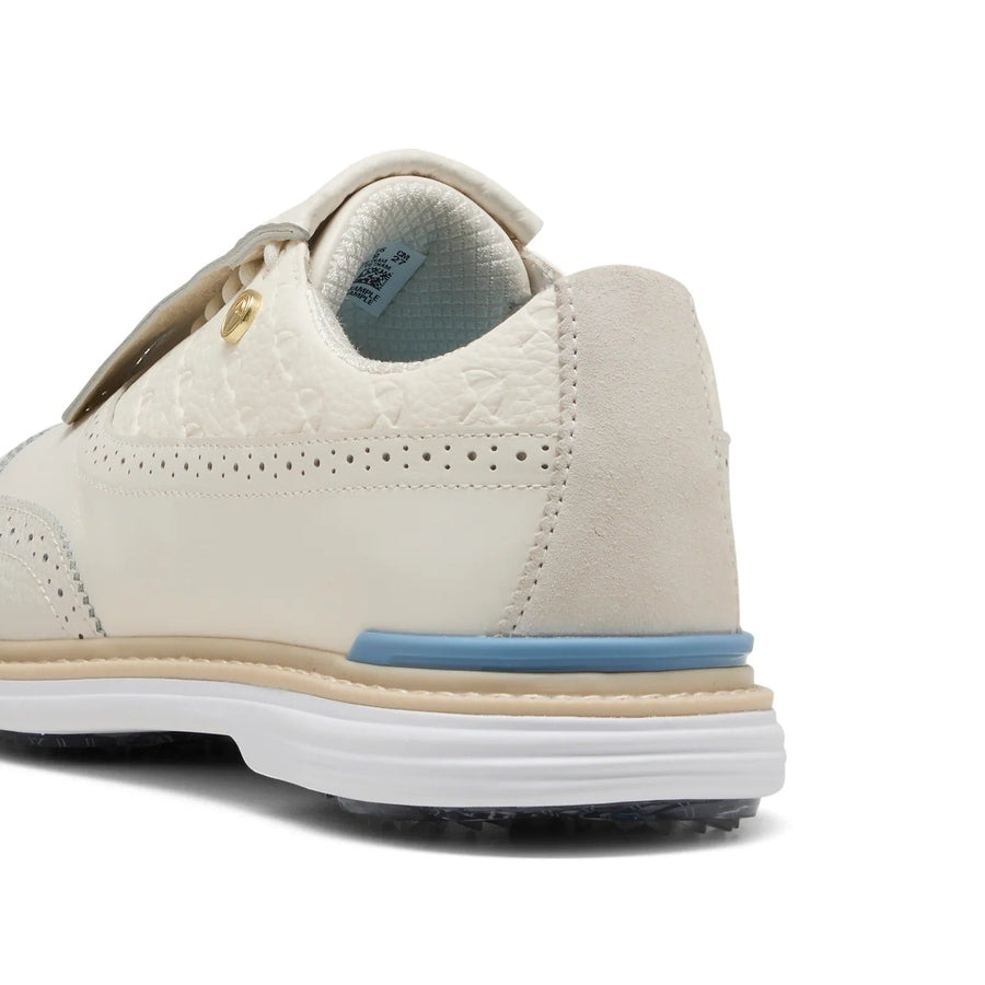 Close-up of the back and side of the Puma Arnold Palmer Royale Wingtip Golf Shoes - Ivory, featuring textured full-grain leather, beige suede heel, tan and blue sole accents, and a spikeless white outsole.