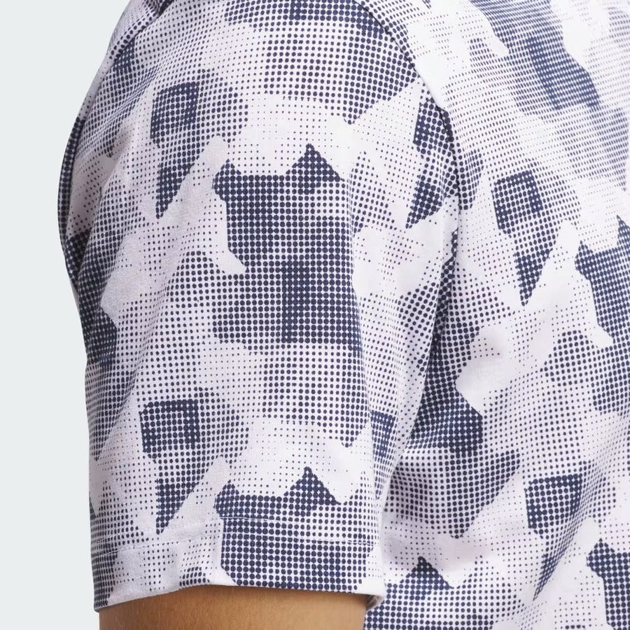 Close-up of a person’s shoulder and upper arm wearing the Adidas 2025 Go-To Printed Polo Shirt, featuring a blue and white abstract geometric dot pattern. Made with recycled materials. The background is plain and light-colored.