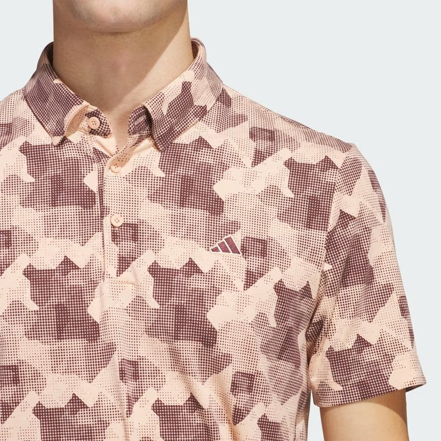 A person wears the Adidas 2025 Go-To Printed Polo Shirt in a pink and brown pattern, featuring a small chest logo and made from recycled materials. The image shows their upper torso and neck, with the full face out of frame.