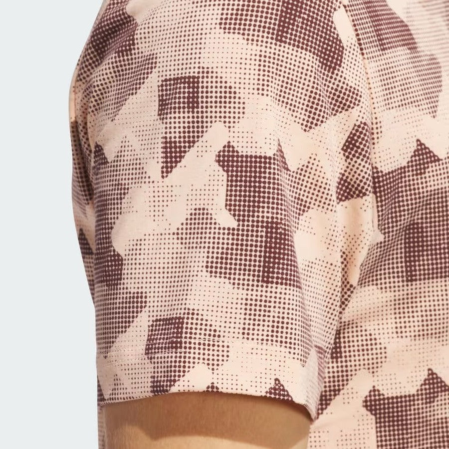 A close-up of the Adidas 2025 Go-To Printed Polo Shirt, a men's short-sleeve golf shirt with a light pink and brown abstract, pixelated design. Made from recycled materials, the fabric and sleeve seam are shown next to the wearer’s arm.